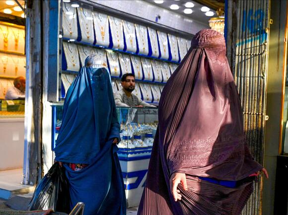 Afghan burqa-clad women walk past jewellery shops at a market in Kandahar on 25 August 2024 (AFP)